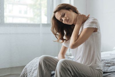 mulher sentada na cama com dor no pescoço